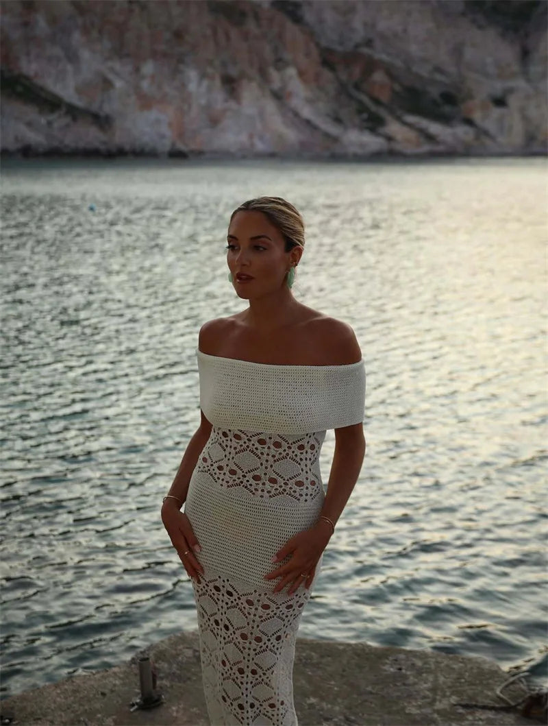 Woman in a white lace dress standing by a body of water with mountains in the background