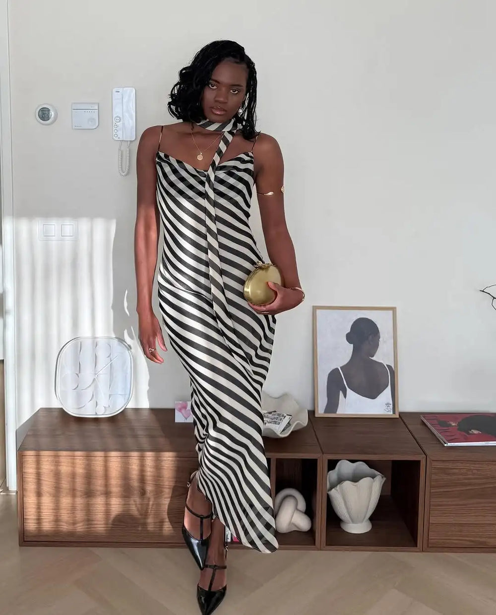 Woman in a black and white striped dress standing in a room with wooden shelves and decor.