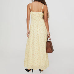 Woman wearing a yellow floral dress holding a brown handbag on a plain background