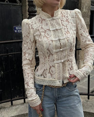 Person wearing a lace blouse with long sleeves and a high collar, standing outdoors.