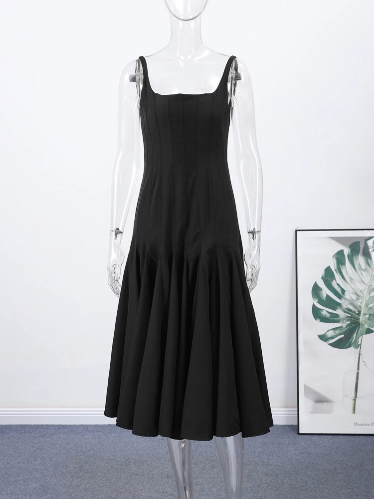 Black dress on a mannequin against a white wall with a framed picture of a plant.