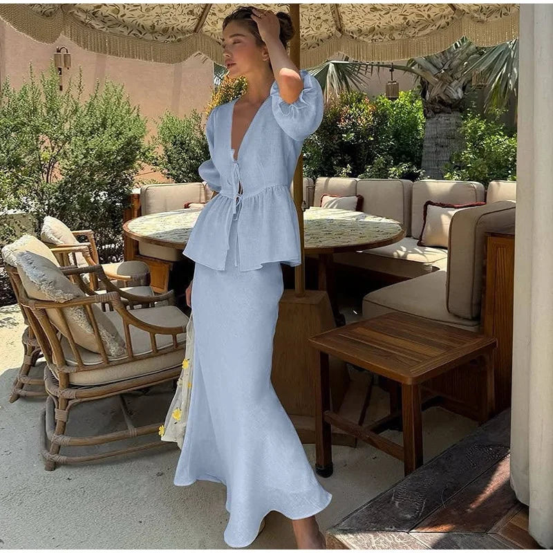 Woman in a light blue dress standing in an outdoor setting with tables and chairs.