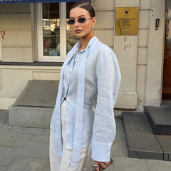 Woman in light blue shirt and beige pants standing on a street with a building in the background