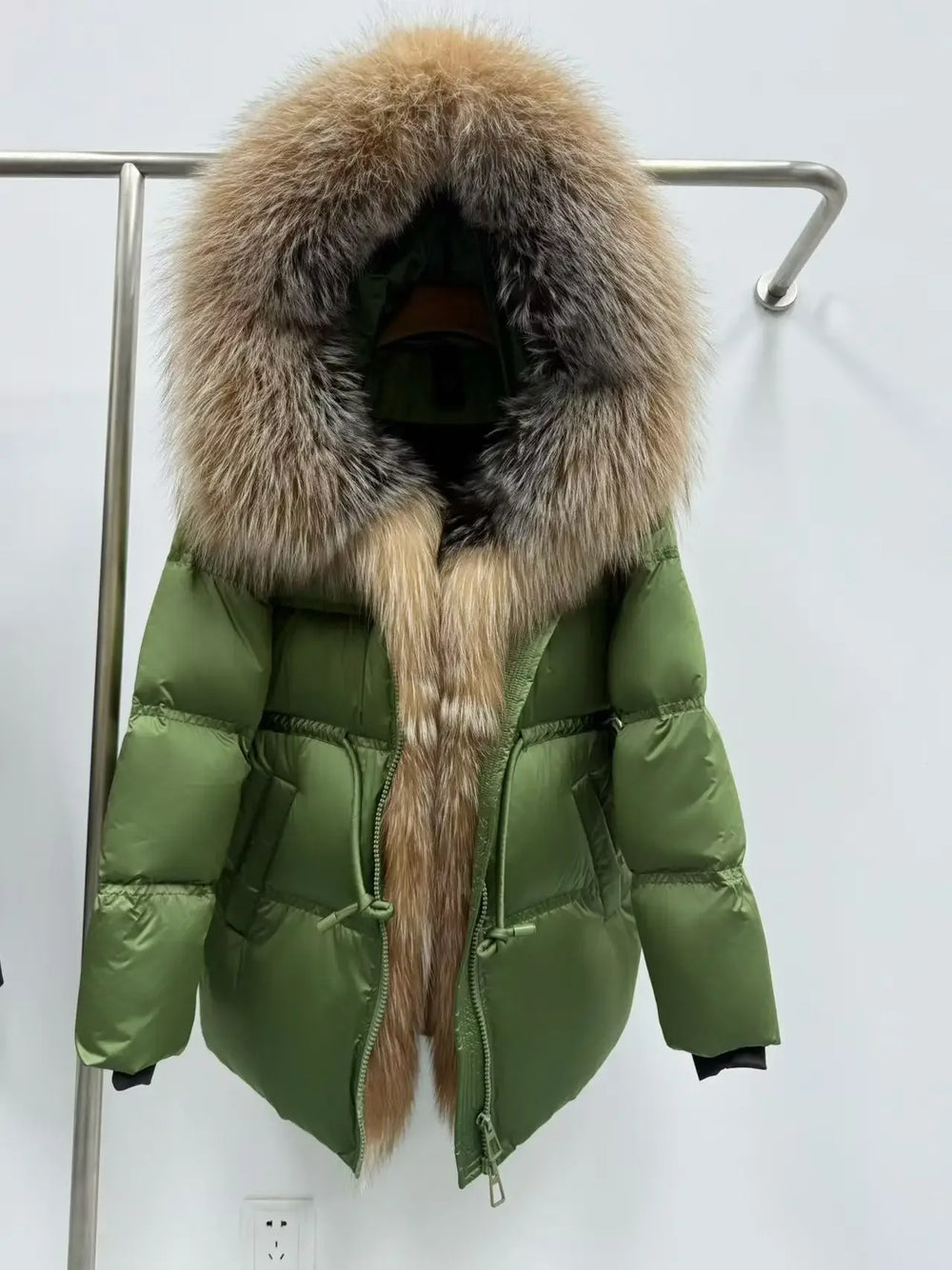 Green puffer jacket with fur hood on a rack against a white background