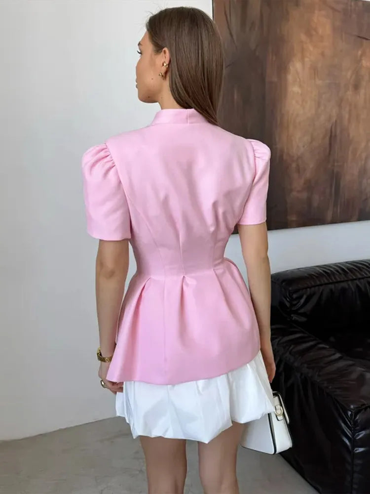 Woman wearing a pink peplum top over a white skirt in an indoor setting.
