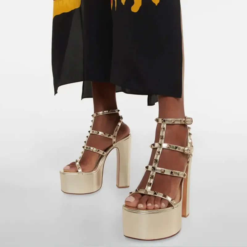 Gold platform sandals with studded details worn by a person in a black dress.
