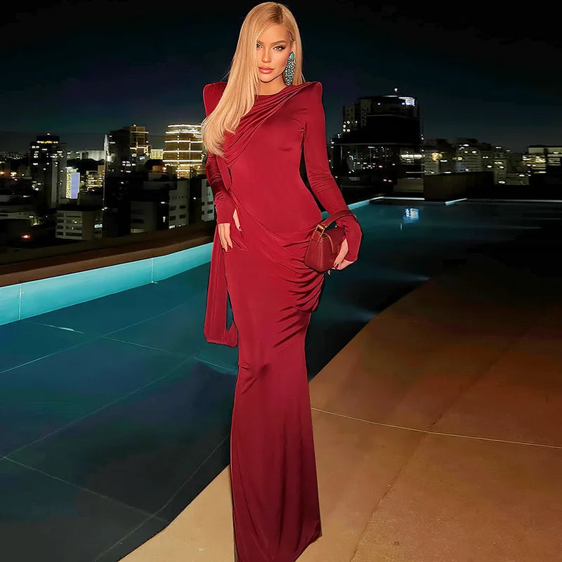 Woman in a red dress standing by a pool with city skyline at night