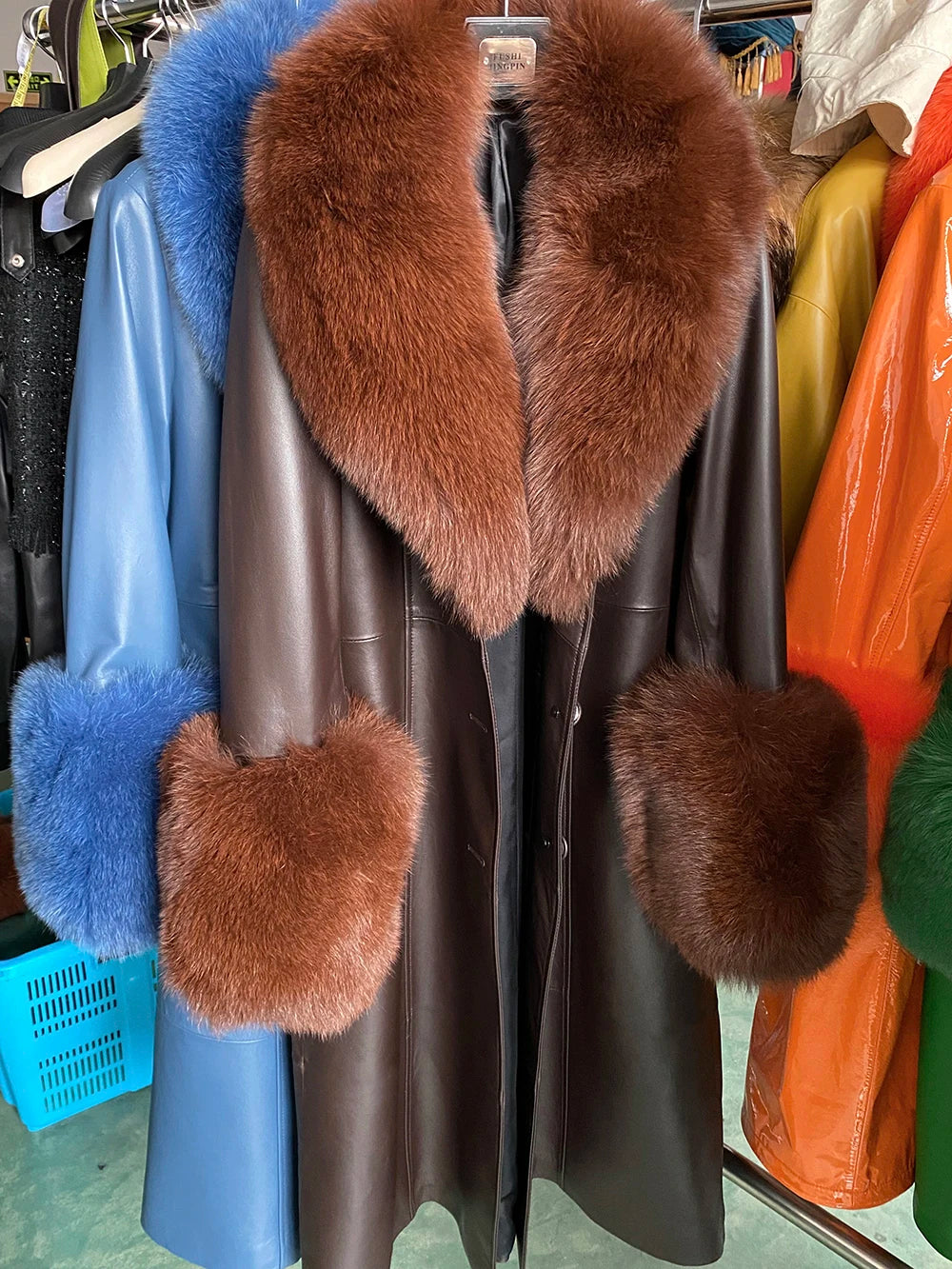 Brown fur-trimmed leather coat on a rack with other colorful coats.