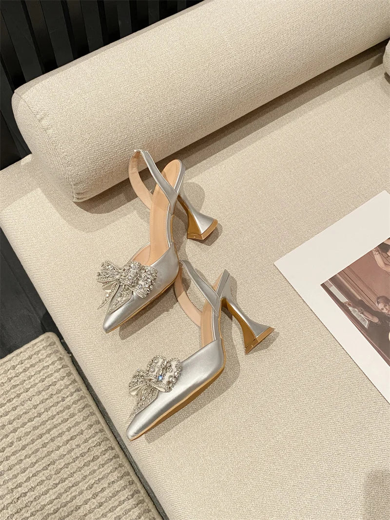 Silver high-heeled shoes with embellishments on a beige surface.