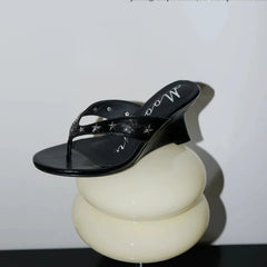 Black wedge sandal with star embellishments on a display stand