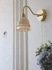 Wall-mounted lamp with decorative glass shade and brass fixture on a white wall.
