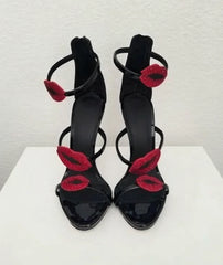 Front view of black patent leather stiletto sandals with red lip embellishments