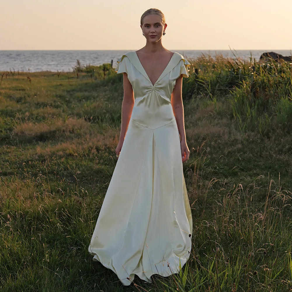 Woman in a white dress standing in a grassy field with a sunset or sunrise in the background.
