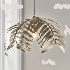 A dramatic iron palm leaf chandelier hanging in a modern dining room with natural light streaming in. A