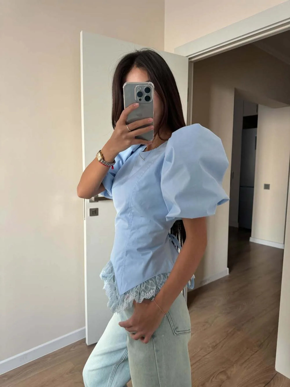 Person wearing a light blue top with puffed sleeves and lace details, standing in a room.