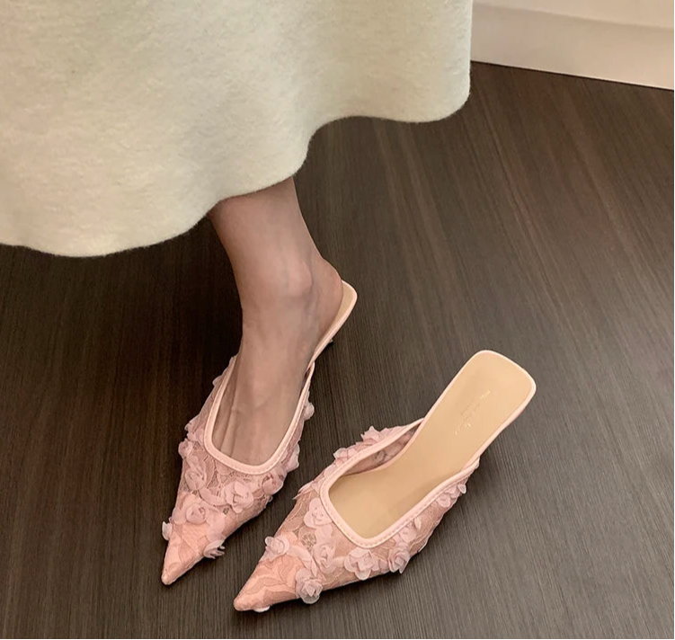 Pink pointed-toe shoes with floral details on a wooden floor