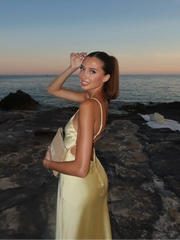 Woman in a yellow dress standing on a rocky beach at sunset