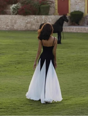 Woman in a black and white dress standing on a grassy field with a horse in the background.