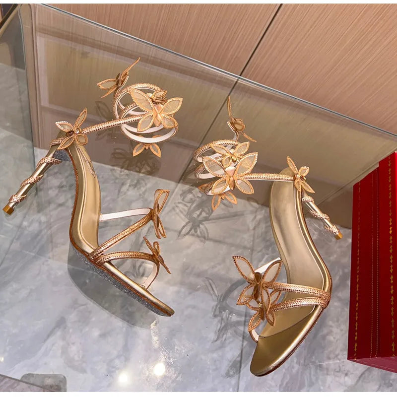 Gold high-heeled shoes with floral designs on a reflective surface