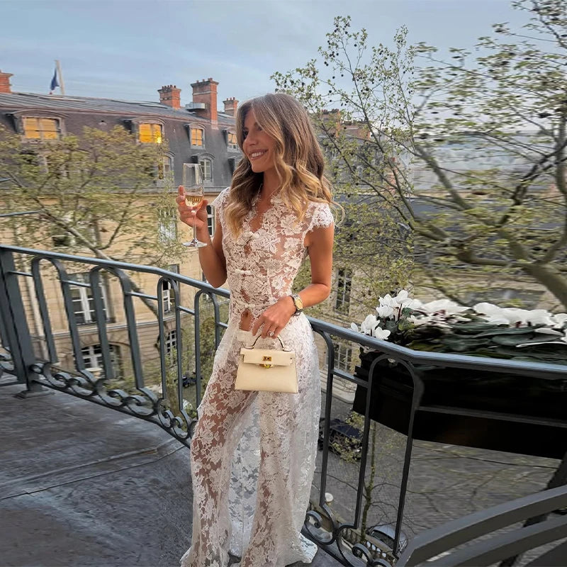 Woman in white lace sleeveless top and wide leg pants holding wine on balcony