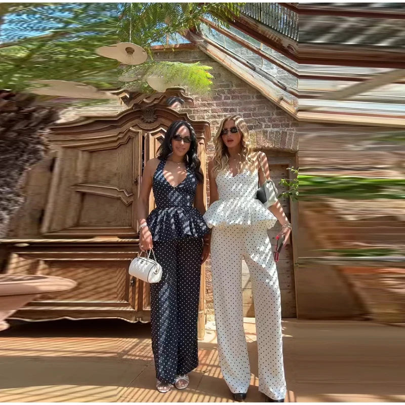 Two women posing outdoors with a decorative wall and plants in the background