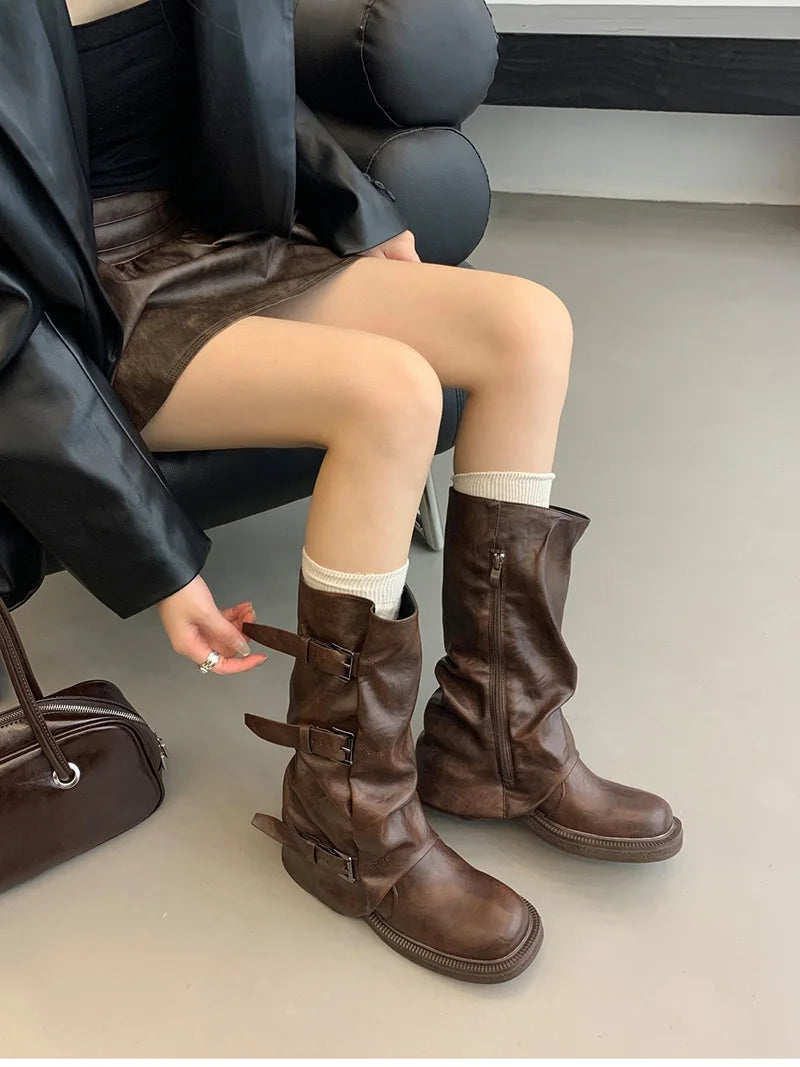 Person wearing brown knee-high boots with a plain background