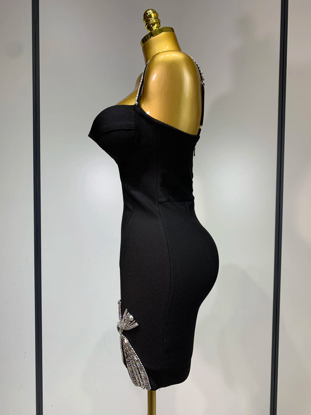 Black dress on a gold mannequin against a plain background