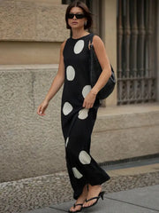 Woman wearing a black sleeveless dress with white polka dots, walking on a street.
