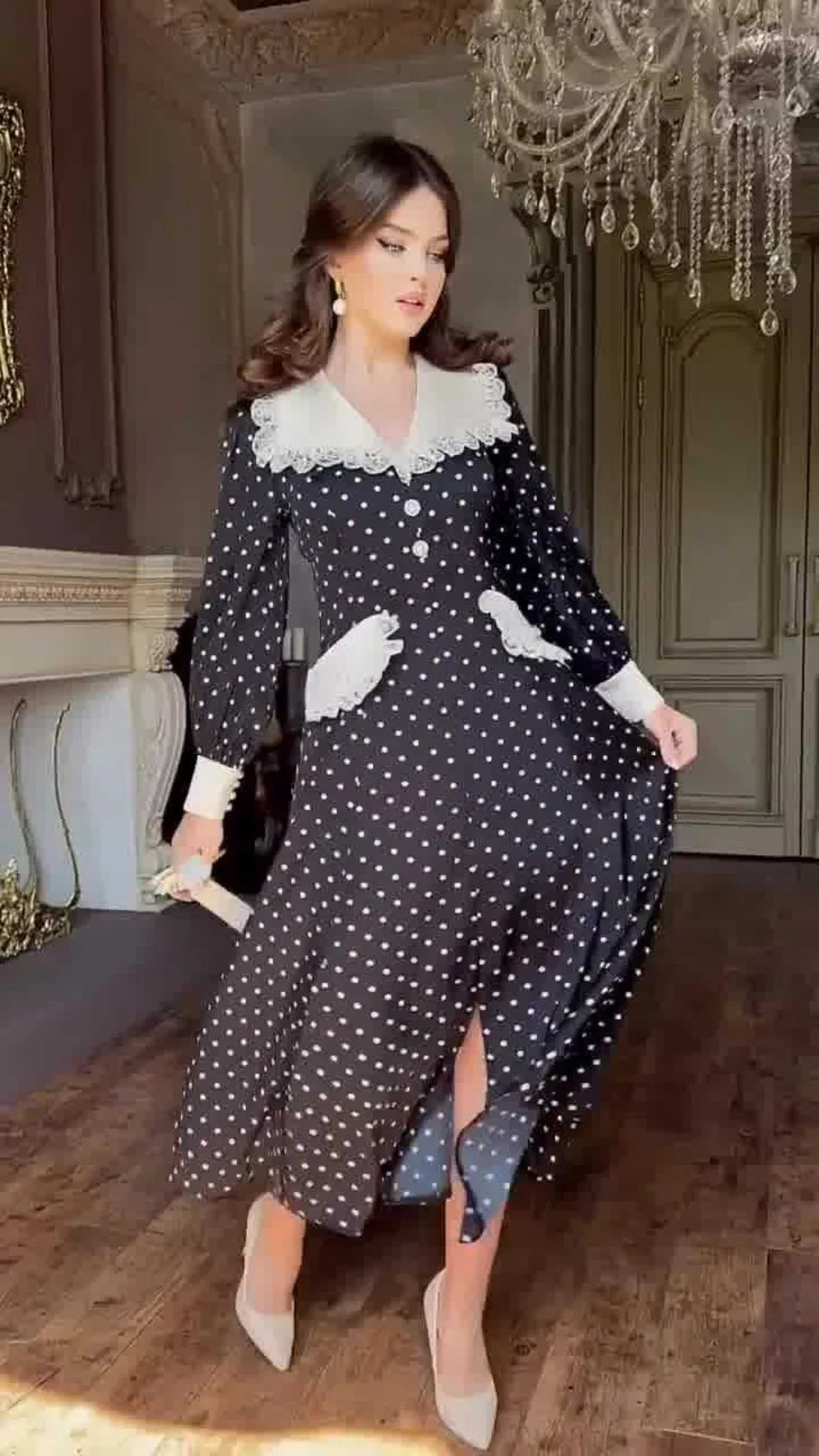 Woman in a black polka dot dress with white lace collar in an elegant room.