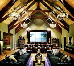 Luxurious home theater with high vaulted ceiling, chandeliers, and large screen.