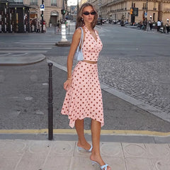 Model wearing pink polka dot halter crop top and asymmetric midi skirt in urban setting.