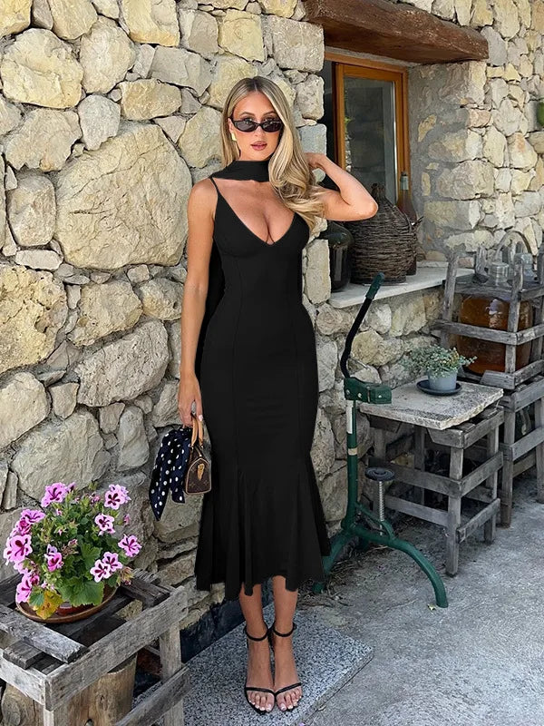 Woman in a black dress standing against a stone wall with outdoor furniture and plants.
