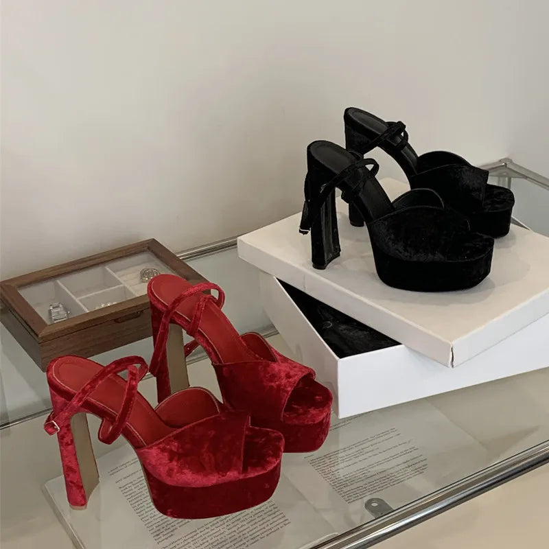 Red velvet high-heeled shoes on display with a black pair of high-heeled shoes in the background.
