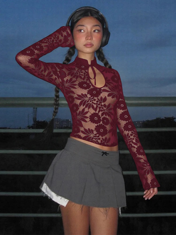 Person wearing a burgundy lace top and gray pleated skirt against a dark background