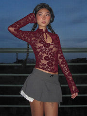 Person wearing a burgundy lace top and gray pleated skirt against a dark background