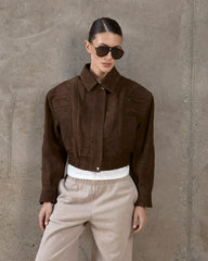 Person wearing a brown jacket and beige pants against a gray concrete wall