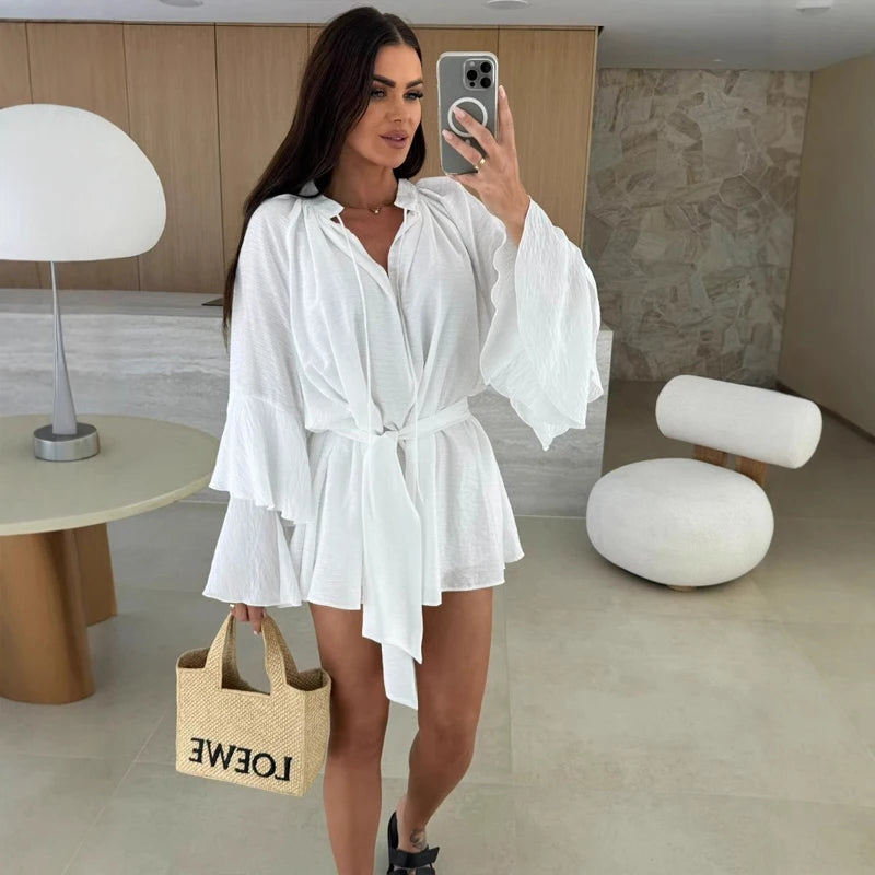 Woman in a white outfit taking a mirror selfie in a modern room.