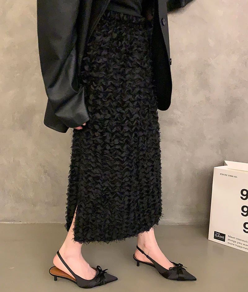 Person wearing a black textured skirt with black shoes on a gray floor.