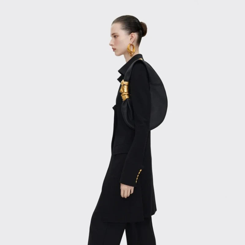 Model carrying a black grained leather half moon shoulder bag with sculpted gold face hardware