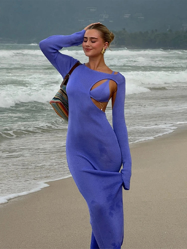 Woman in a blue dress standing on a beach with ocean waves in the background