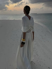 Woman in a white dress standing on a beach at sunset