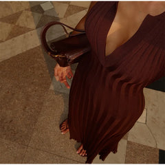 Person wearing a brown pleated dress holding a matching handbag on a patterned floor.