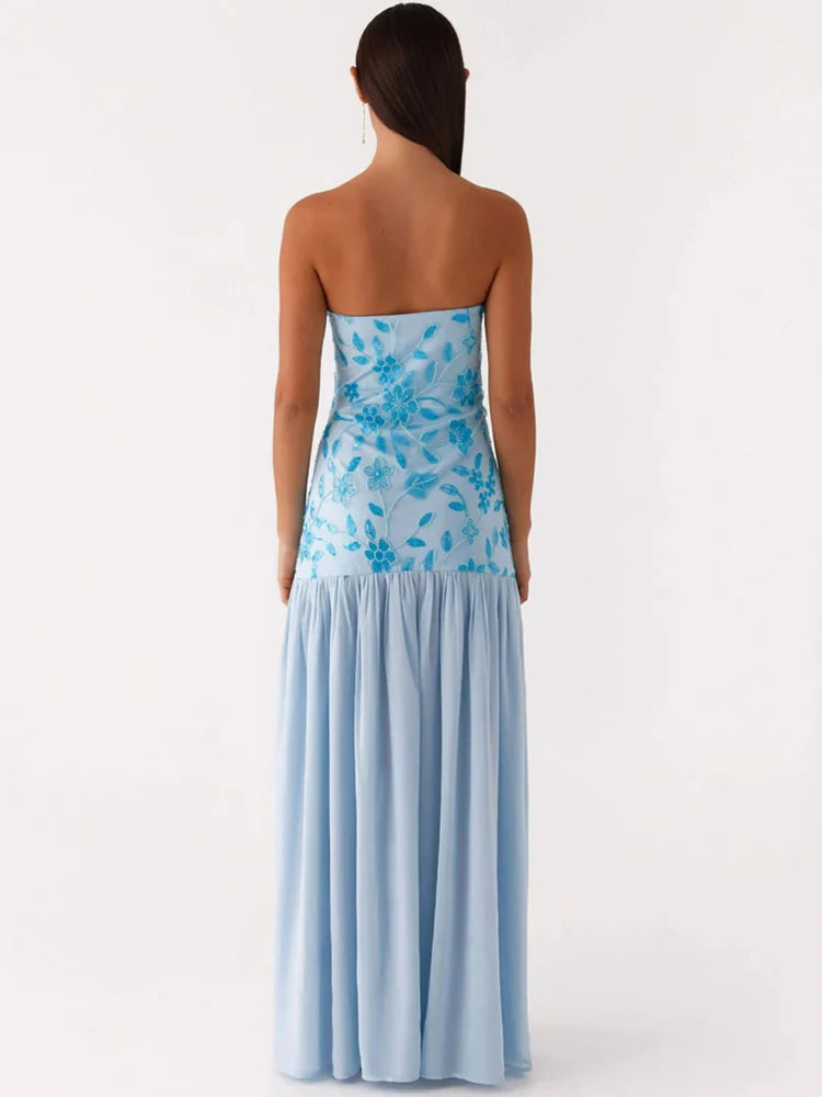 Woman wearing a strapless dress with blue floral top and light blue skirt on a white background