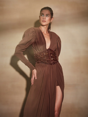 Woman wearing a brown evening gown with a slit on a beige background