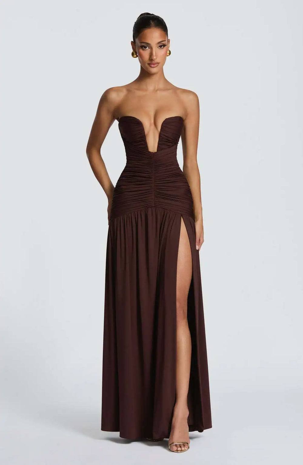 Woman wearing a strapless brown evening gown with a high slit on a white background