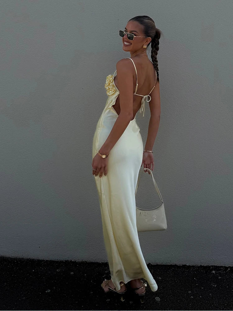 Woman in a white dress with floral details, holding a white handbag against a plain background