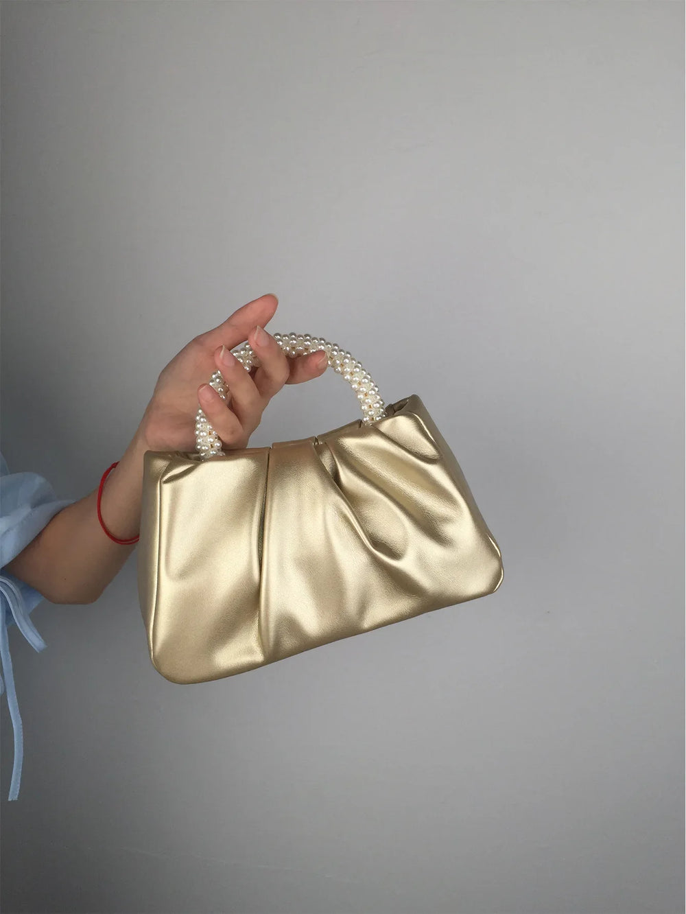 Hand holding a pink gathered clutch bag with a pearl handle