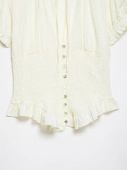 Close-up of a cream-colored blouse with ruffled details on a white background