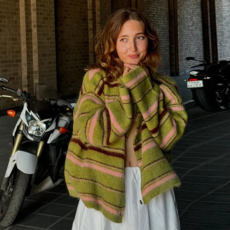 Woman wearing a green and pink striped sweater standing in front of motorcycles.
