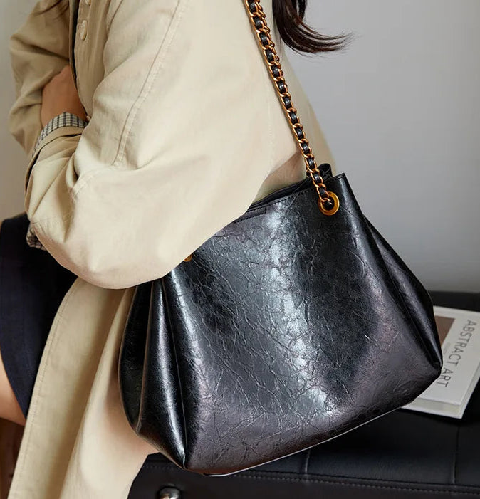 Person holding a black leather handbag with a gold chain strap.